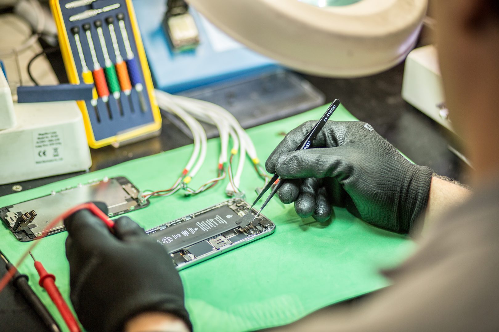 Técnico reparando placa lógica iPhone con pinzas en taller Teveotecno